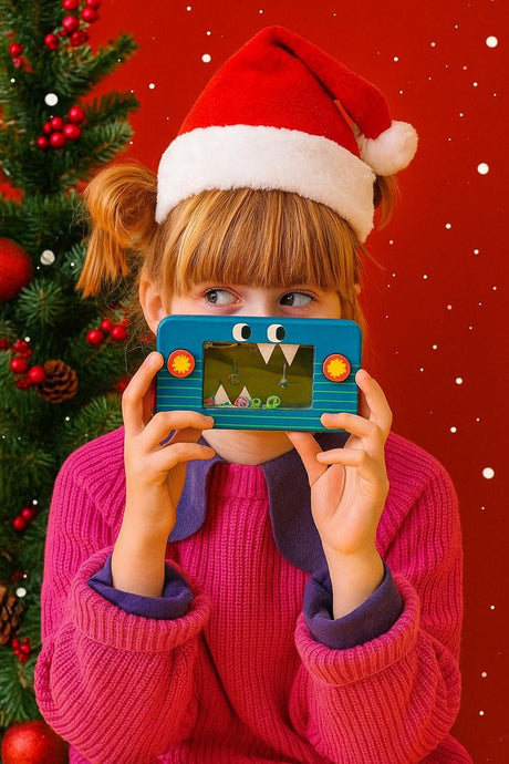 A girl in a Santa hat holds a blue toy in front of her face with a Christmas tree and snowflakes behind her.