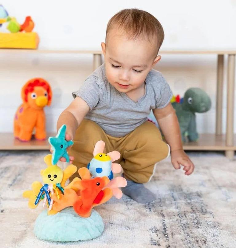 Toddler sitting on a rug playing with colorful soft developmental toys designed to support early learning and sensory development.