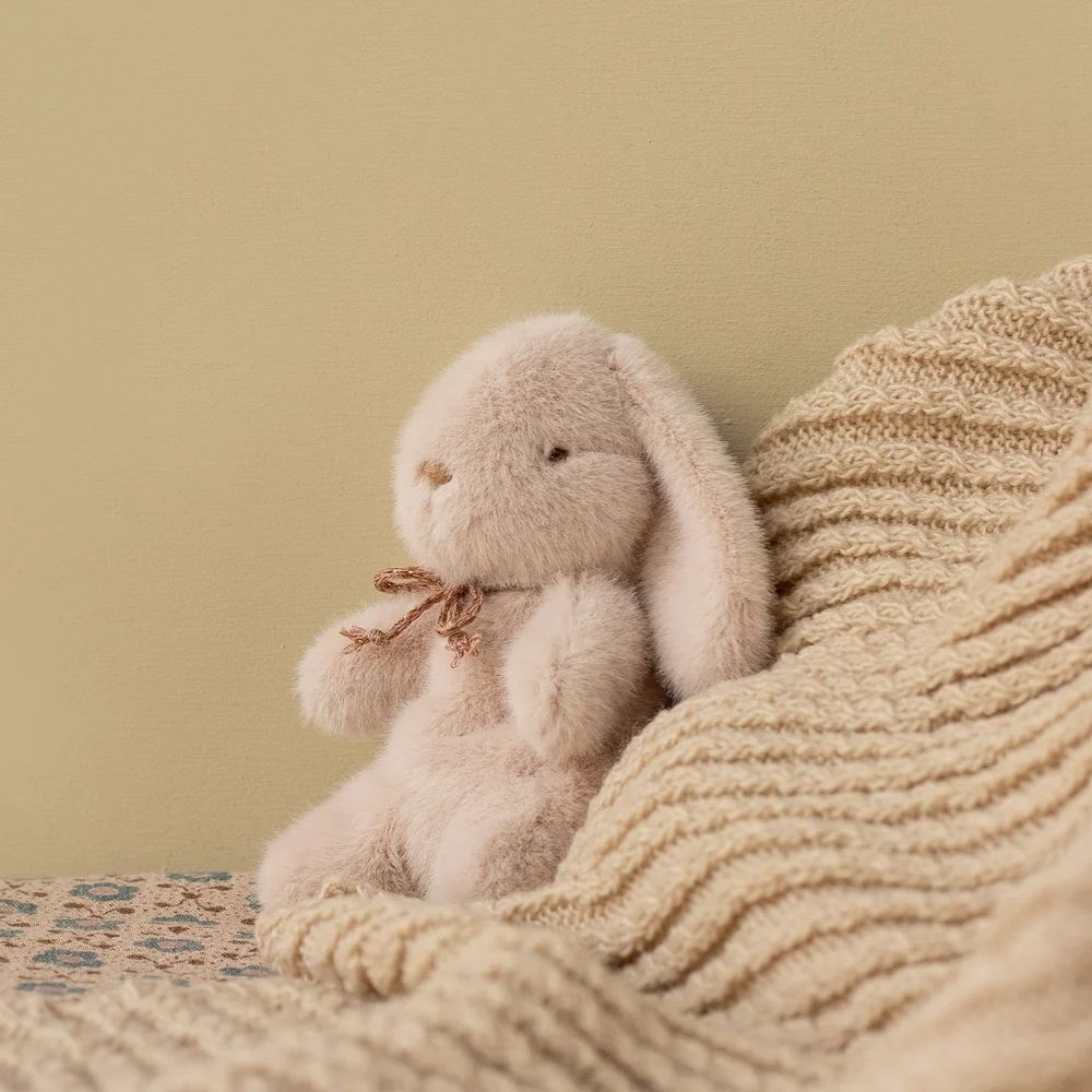 Plush bunny toy with a bow sitting on a textured surface against a beige wall.